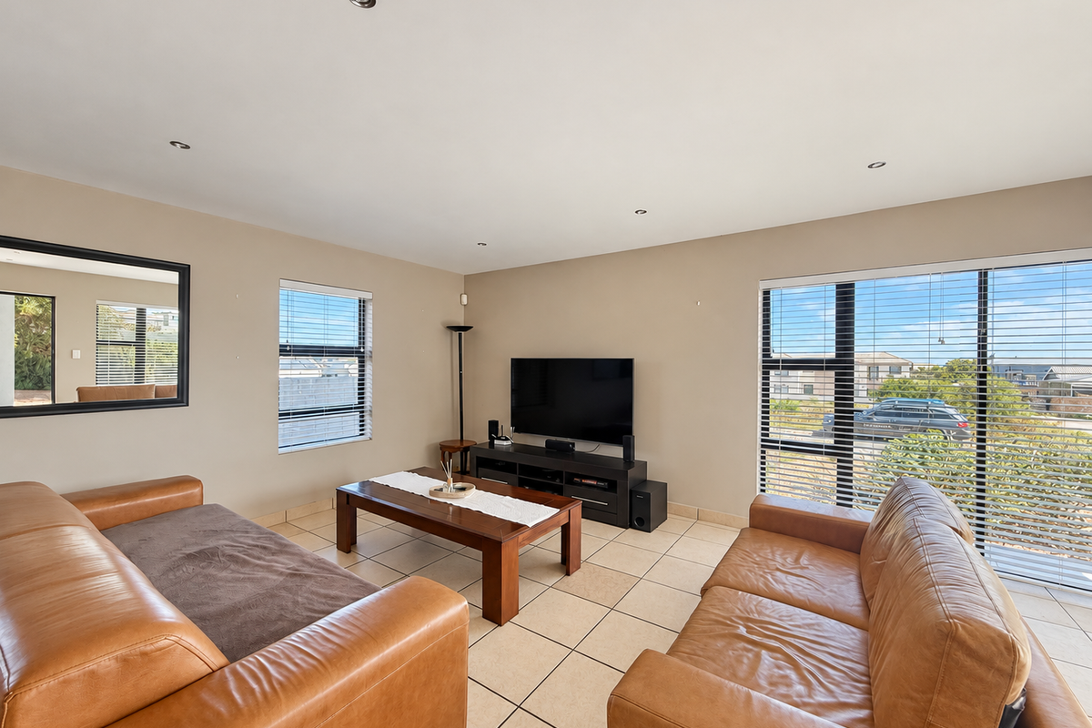 A bright and spacious living room featuring neutral walls, tiled flooring, recessed downlights, and large windows with aluminium frames providing natural light.