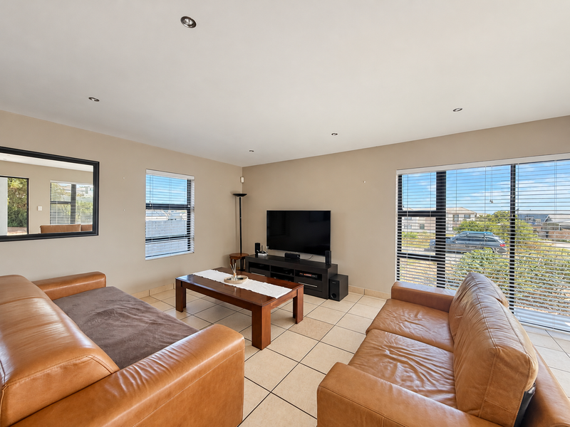 A bright and spacious living room featuring neutral walls, tiled flooring, recessed downlights, and large windows with aluminium frames providing natural light.