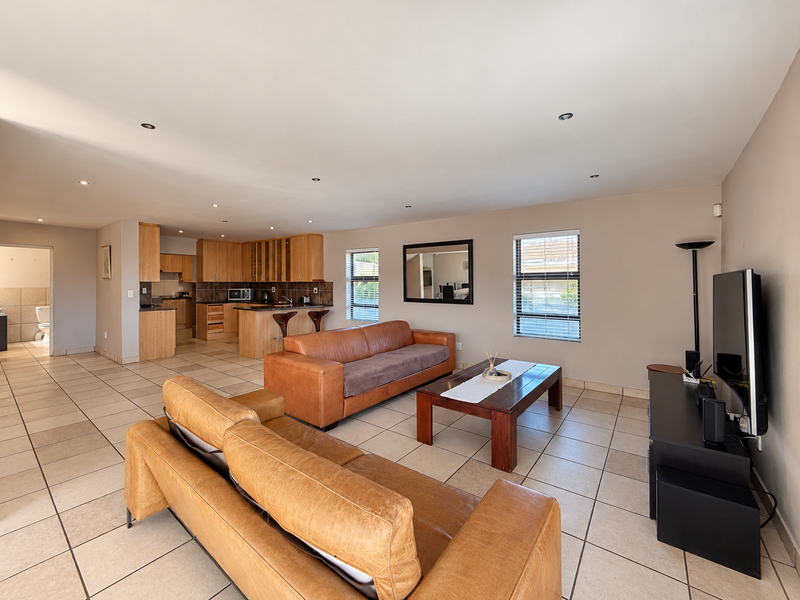 Spacious open-plan living area featuring tiled floors, recessed lighting, and a functional kitchen with wooden cabinetry and granite countertops.