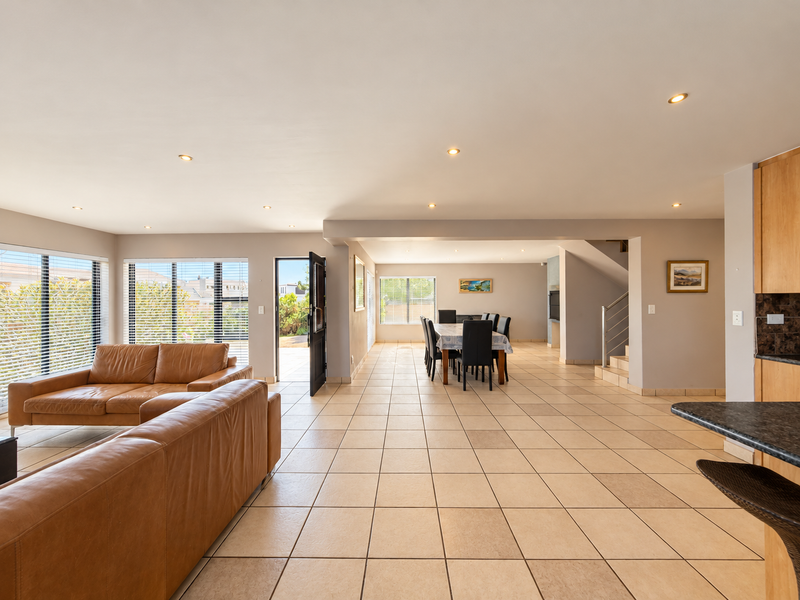 Spacious open-plan living and dining area featuring neutral tiled flooring, recessed lighting, and a modern staircase, creating a bright and functional family space.