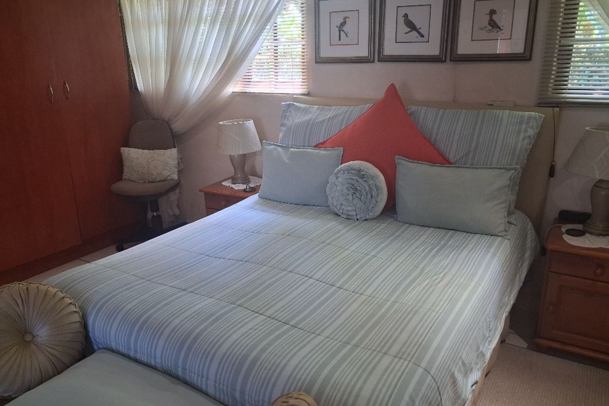 A cozy bedroom featuring a built-in wardrobe, air conditioning unit, and venetian blinds, offering a functional and comfortable living space.