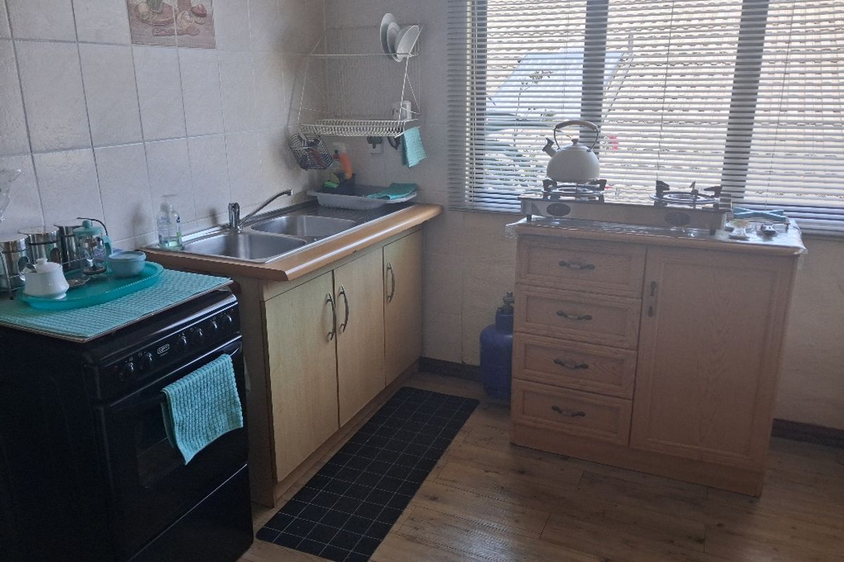 A functional kitchen area featuring laminate cabinetry, a double sink, gas stove, and tiled backsplash with wood-look laminate flooring.