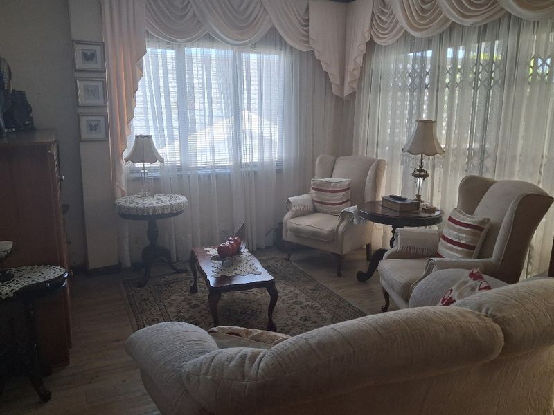 A cozy living room featuring laminate flooring, large windows with decorative pelmets, and integrated security gates, offering a comfortable and traditional living space.