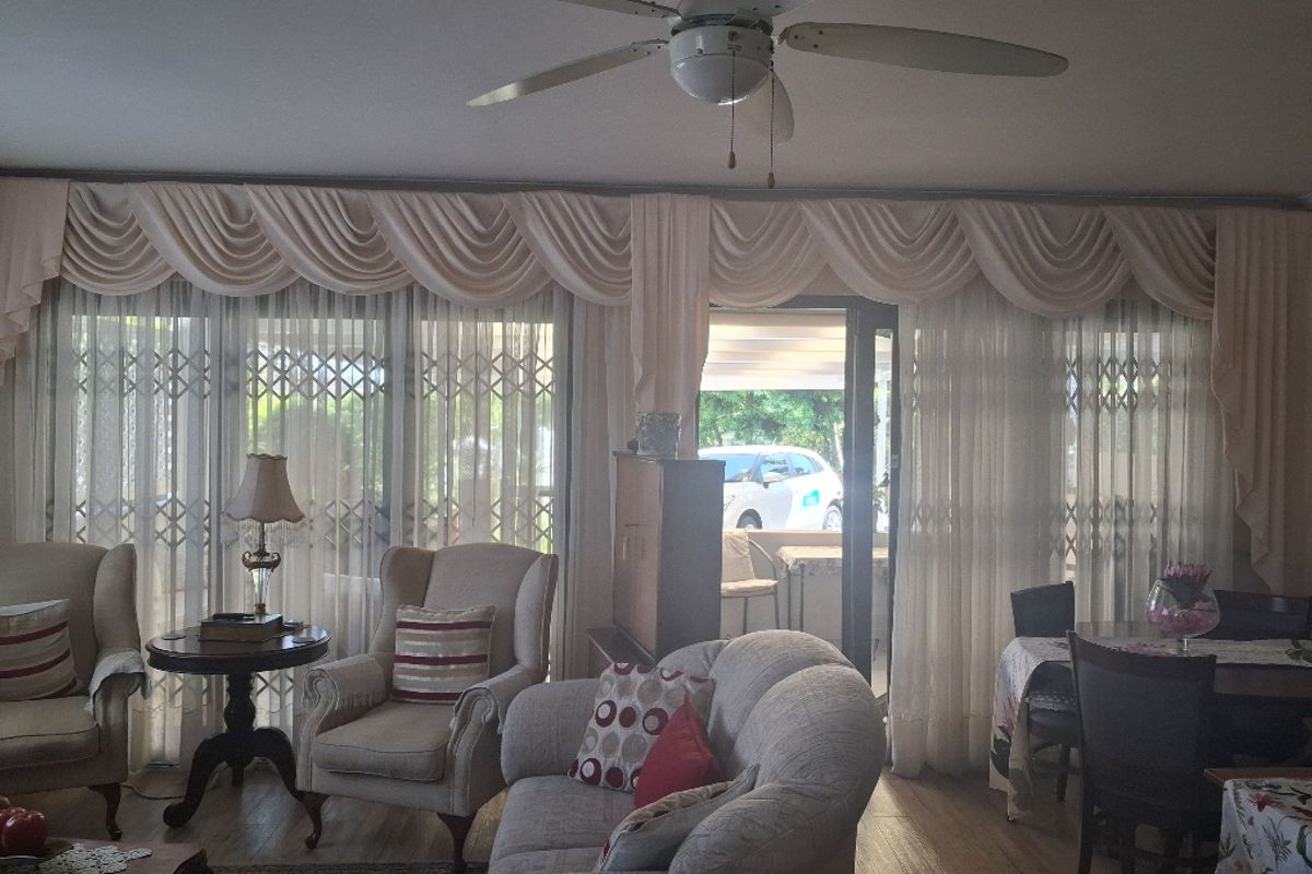 A comfortable living room featuring laminate flooring, a ceiling fan, and large sliding glass doors with security gates leading to the exterior.