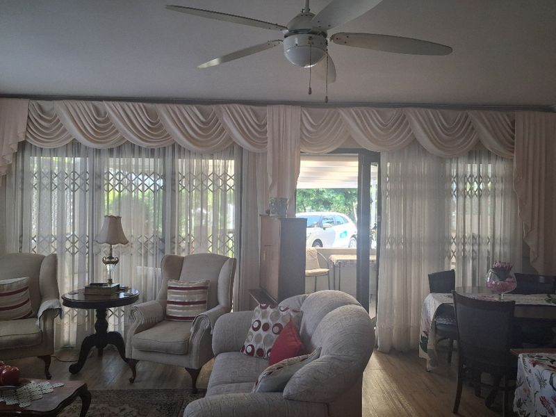 A comfortable living room featuring laminate flooring, a ceiling fan, and large sliding glass doors with security gates leading to the exterior.