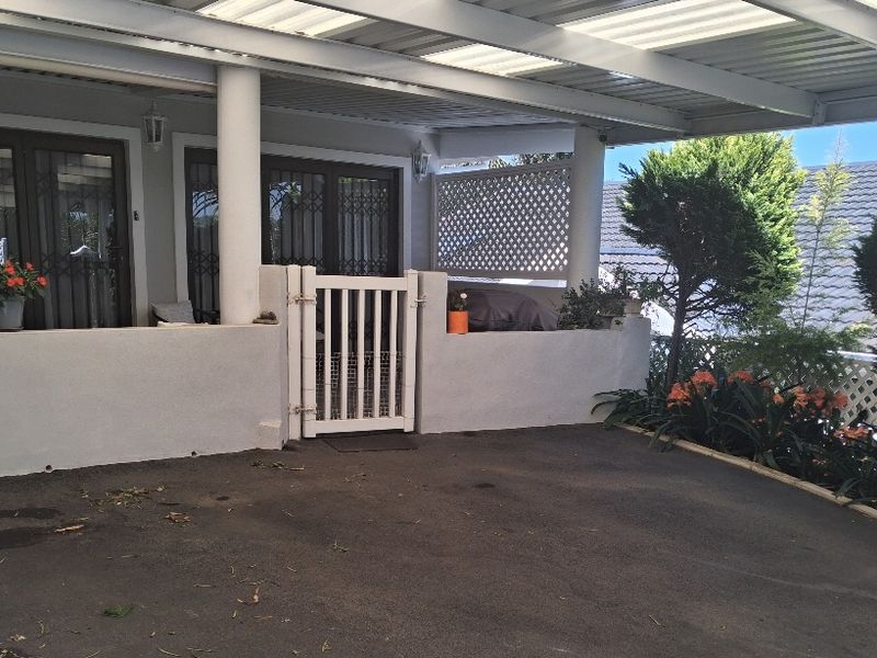 A covered patio area featuring a low wall, security gates, and a lattice privacy screen, providing a functional outdoor space for the cottage.