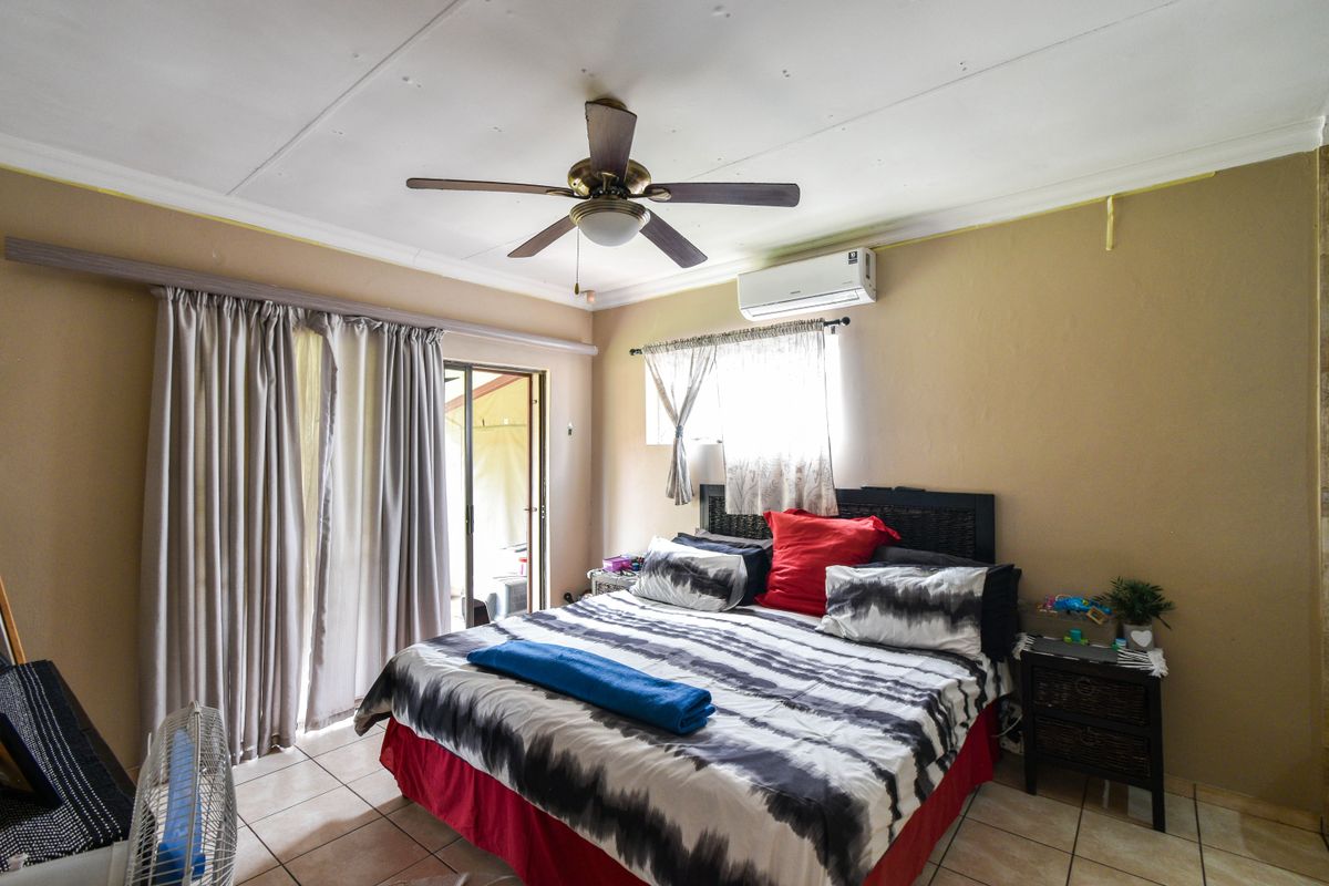A bedroom featuring tiled flooring, a ceiling fan, and a wall-mounted air conditioning unit, with sliding door access to an outdoor area.