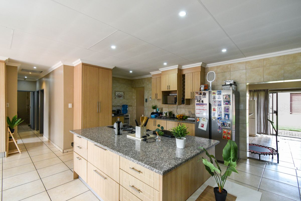 Spacious kitchen featuring a central island with granite countertops, light wood cabinetry, tiled flooring, and recessed ceiling lighting.