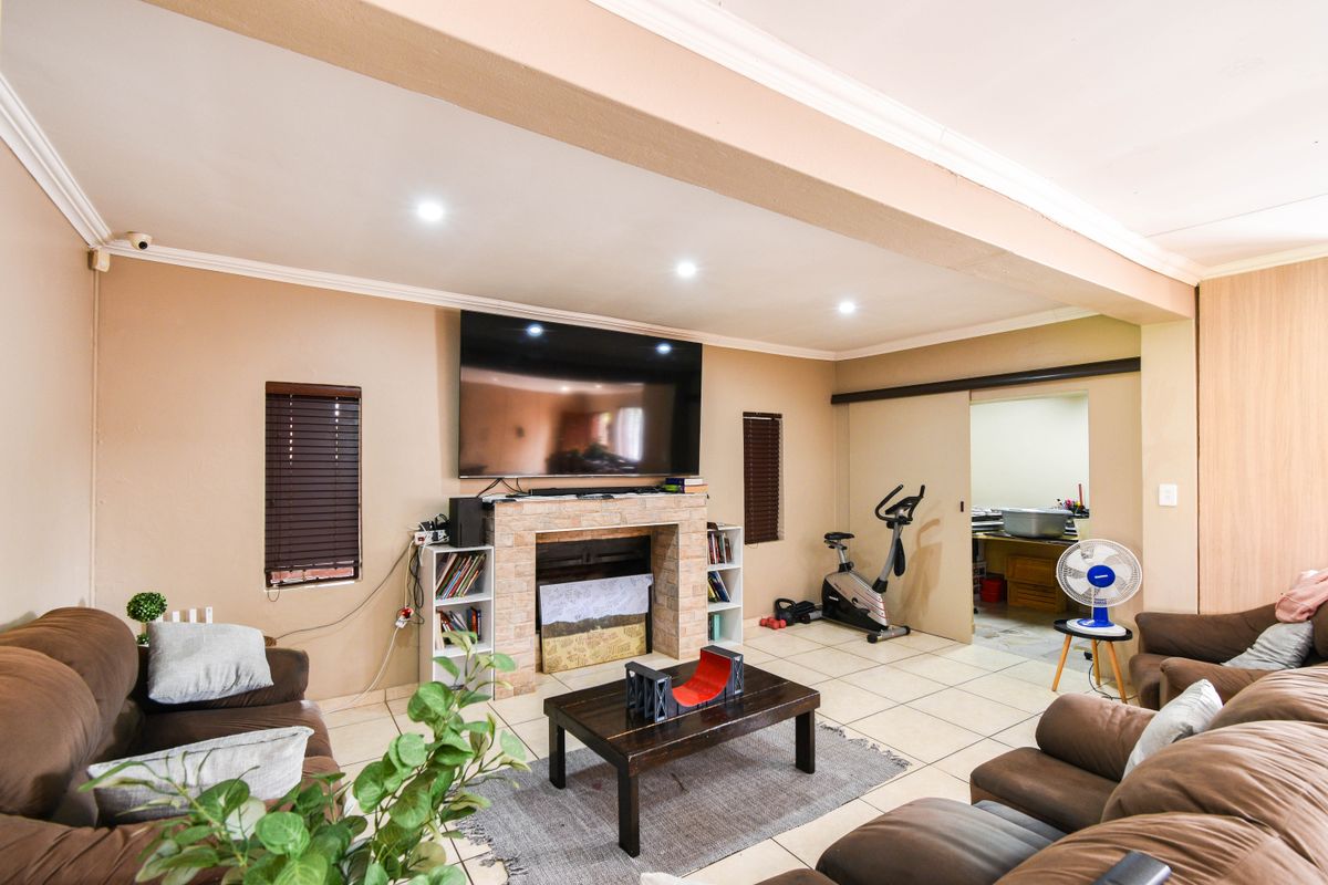 Spacious living room featuring a stone-clad fireplace, tiled flooring, and recessed ceiling lighting, with an adjacent utility area accessible via a sliding door.