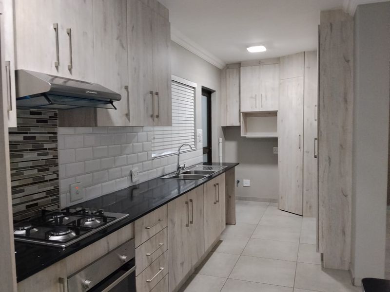 Modern kitchen featuring light wood-grain cabinetry, dark stone countertops, gas hob, built-in oven, and a tiled splashback with a double sink.