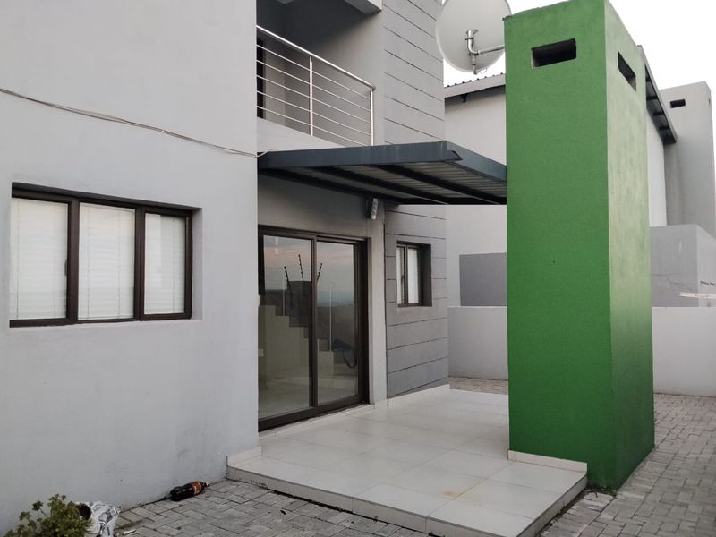 Rear exterior view of the townhouse featuring a paved courtyard, tiled patio area, built-in braai chimney, and a sliding glass door entrance.