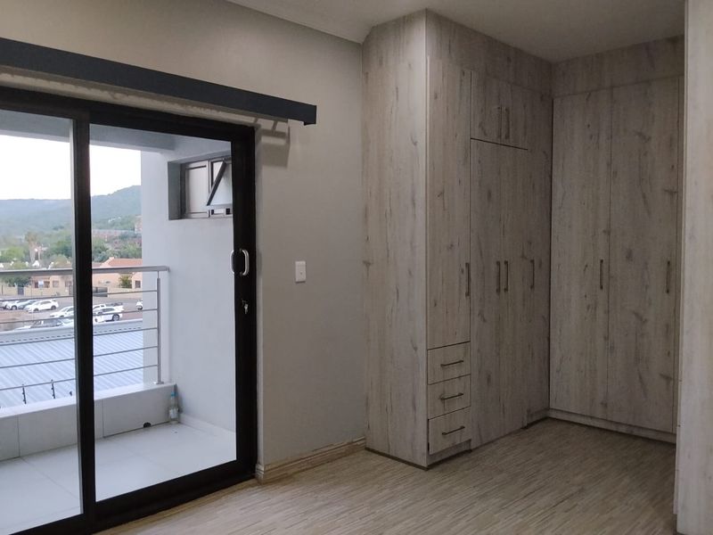 A bright bedroom featuring modern built-in cupboards, laminate flooring, and a sliding glass door leading to a private balcony.
