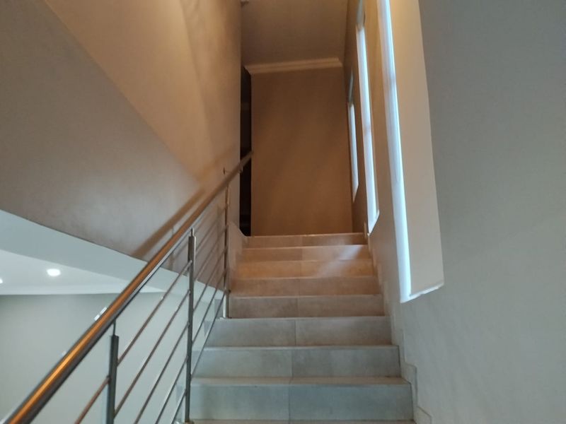 A bright and modern staircase featuring tiled steps and a sleek stainless steel balustrade, leading to the upper level of the townhouse.