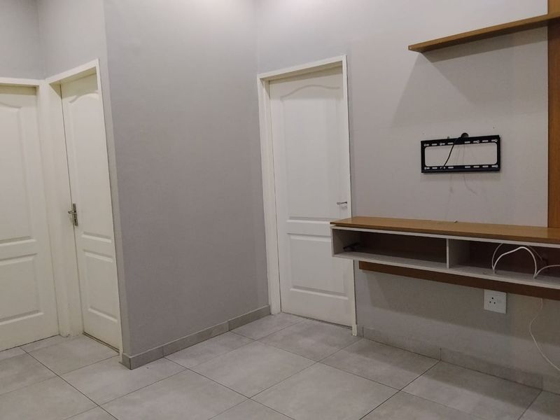 A clean, neutral living area featuring tiled flooring, built-in shelving, and a wall-mounted TV bracket, offering a versatile space ready for personalization.