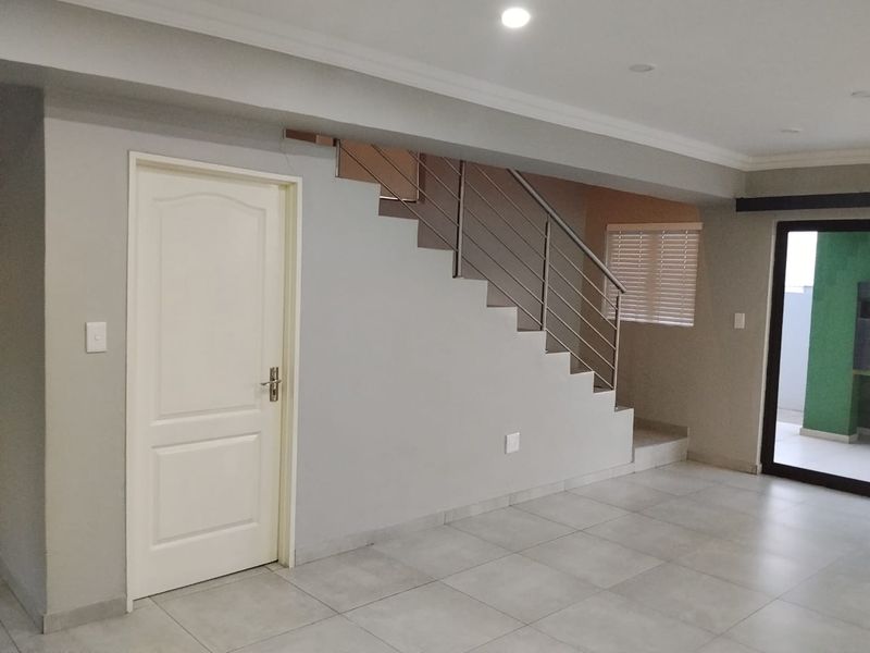 Spacious open-plan living area featuring neutral tiled flooring, a modern staircase with stainless steel balustrades, and direct access to an outdoor patio area.