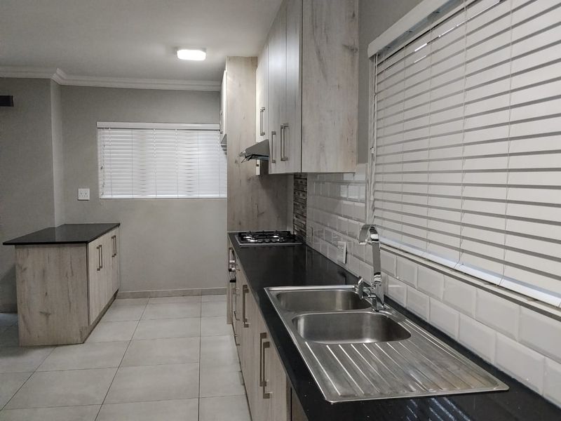 Modern kitchen featuring light wood-grain cabinetry, black countertops, a gas hob, extractor fan, and a double sink with subway tile backsplash.