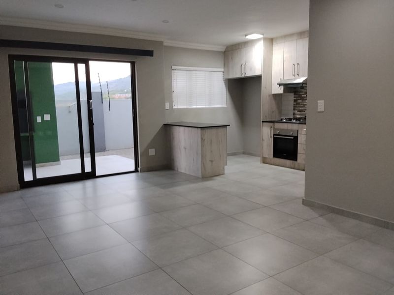 Spacious open-plan living and kitchen area featuring modern cabinetry, built-in appliances, tiled flooring, and direct access to an outdoor patio through sliding glass doors.