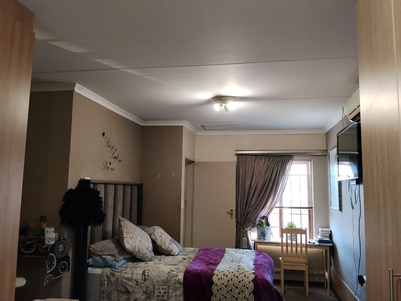 A functional bedroom featuring built-in cupboards, an air conditioning unit, and a window with blinds, providing a comfortable and practical living space.