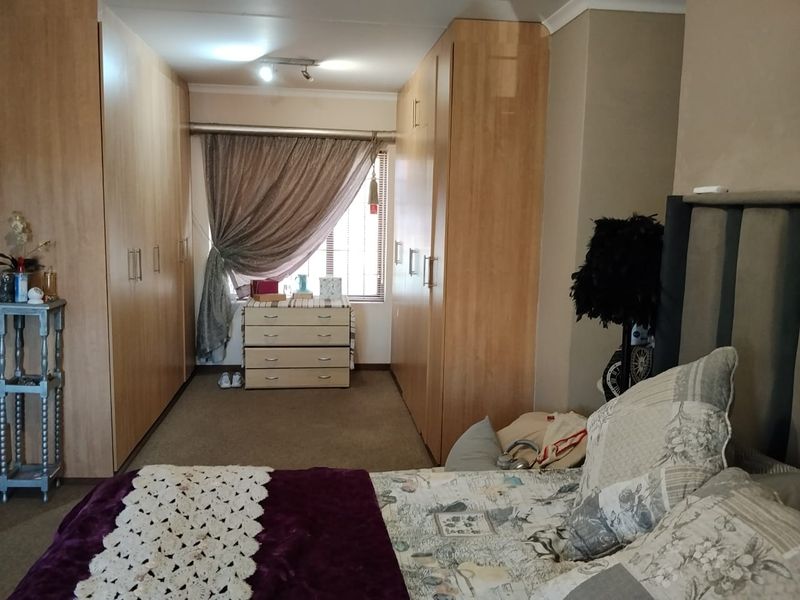 A bedroom featuring extensive built-in wooden cupboards providing ample storage space, carpeted flooring, and a window allowing natural light.