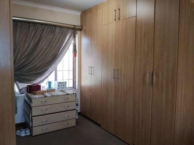 A bedroom featuring extensive floor-to-ceiling built-in wooden cupboards, carpeted flooring, and a window fitted with security bars.