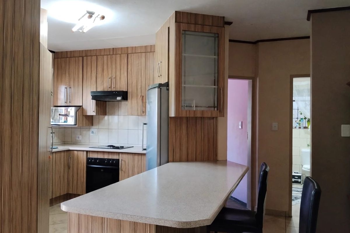 Functional kitchen featuring wood-look laminate cabinetry, built-in oven, electric hob, extractor fan, and a convenient breakfast bar counter.