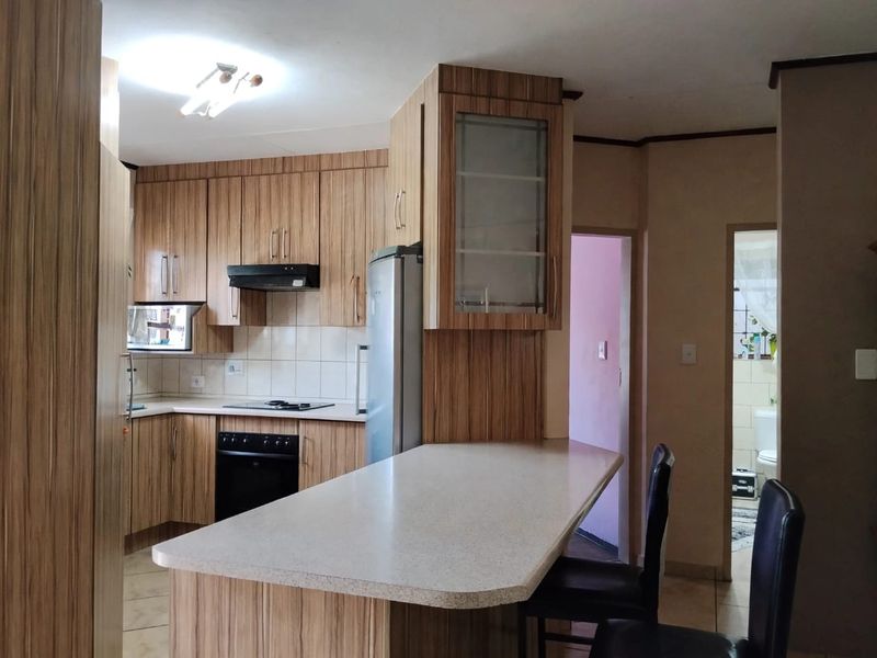 Functional kitchen featuring wood-look laminate cabinetry, built-in oven, electric hob, extractor fan, and a convenient breakfast bar counter.