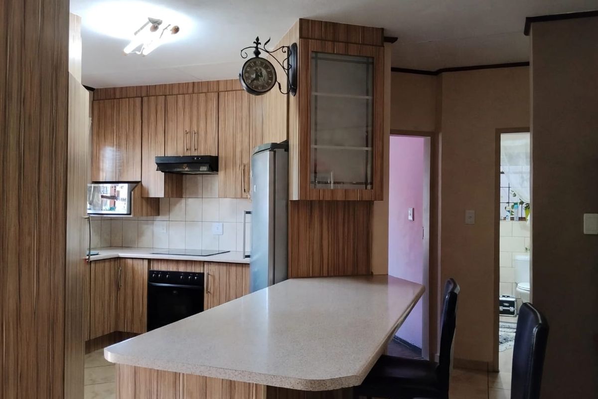 Functional kitchen featuring wood-look laminate cabinetry, a built-in oven with hob, extractor fan, and a convenient breakfast bar island.