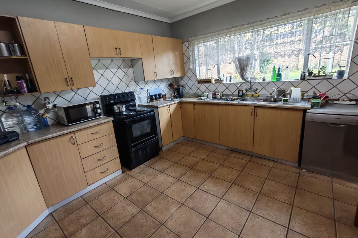 A functional kitchen featuring wood-look laminate cabinetry, a diamond-patterned tile backsplash, ceramic floor tiles, and a built-in oven with hob.