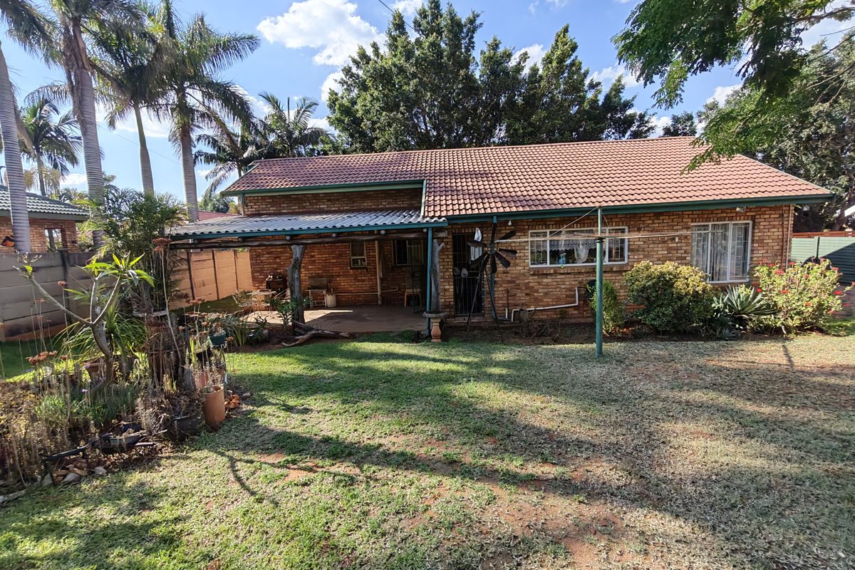 Rear view of a face brick house featuring a covered patio area, tiled roof, and a spacious garden with established trees.