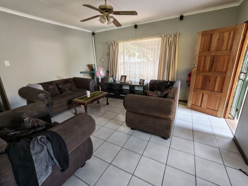A living room featuring tiled flooring, a ceiling fan, and a solid wooden entrance door.
