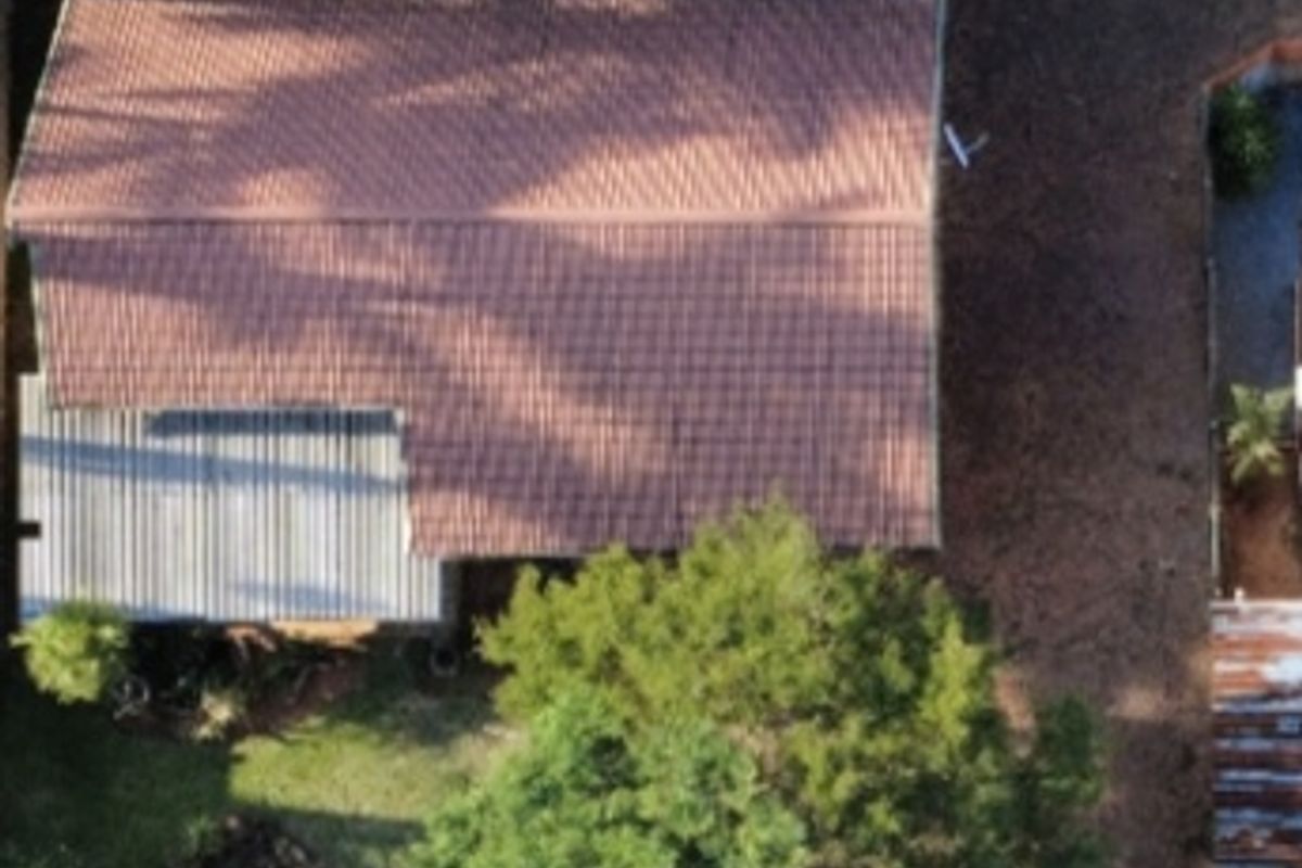 Aerial view of the property showing the main tiled roof structure, secondary corrugated metal roofing, and surrounding garden area with mature trees.