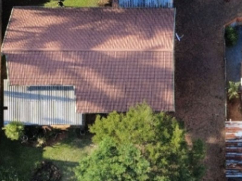 Aerial view of the property showing the main tiled roof structure, secondary corrugated metal roofing, and surrounding garden area with mature trees.