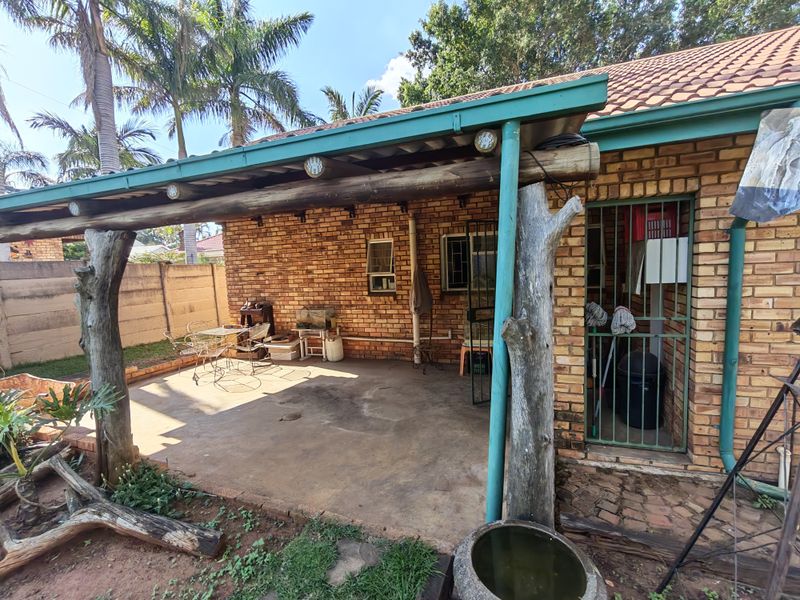 A covered outdoor patio area featuring exposed brickwork, rustic timber support posts, and a concrete floor, providing a functional space for outdoor living.