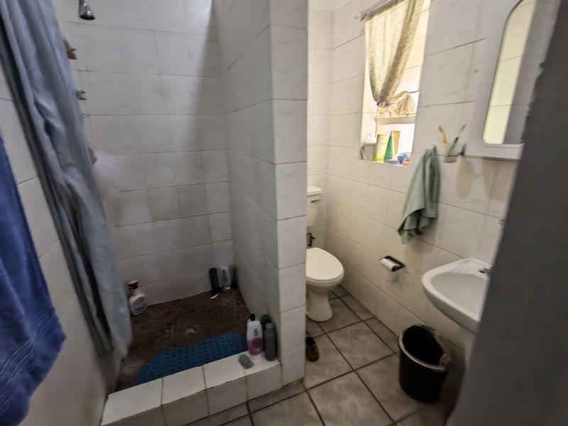 A functional bathroom featuring a shower cubicle, pedestal basin, and toilet with tiled finishes throughout, offering potential for modernization and cosmetic updates.