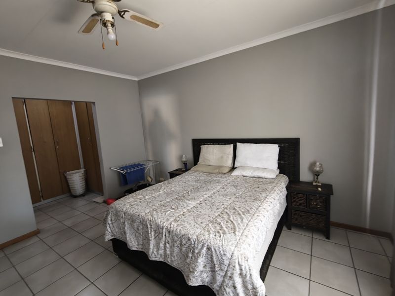 A bedroom featuring tiled flooring, built-in wooden cupboards, and a ceiling fan, providing a functional and neutral living space.