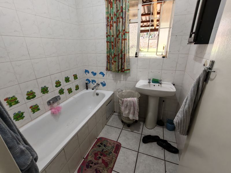 A functional bathroom featuring a built-in bathtub, pedestal washbasin, and tiled finishes. The space would benefit from modern updates to fixtures and decor.