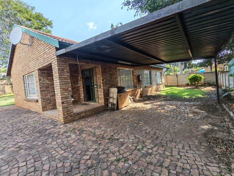 Front exterior view of a face brick house featuring a large paved driveway, covered carport, and established garden area.