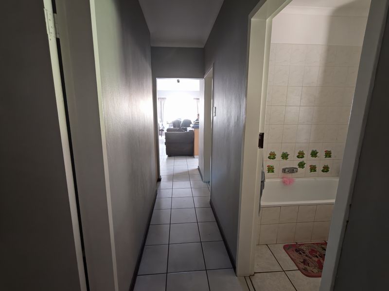 A view down a tiled hallway leading to a living area, with a bathroom visible to the right featuring wall tiles and a built-in bathtub.