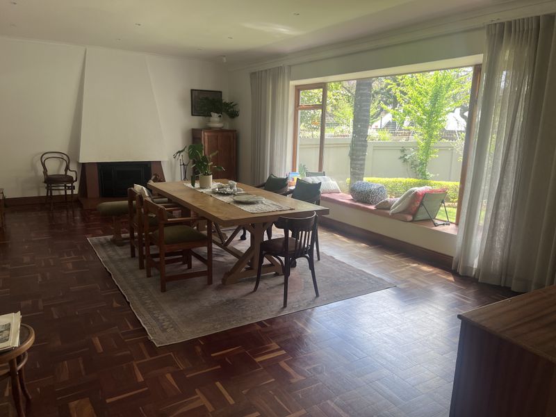 Spacious dining room featuring classic parquet flooring, a built-in fireplace, and a large picture window with a built-in window seat overlooking the garden.