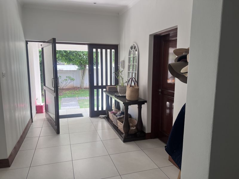 A bright entrance hall featuring tiled flooring, coving, and a timber door leading to the exterior garden area.