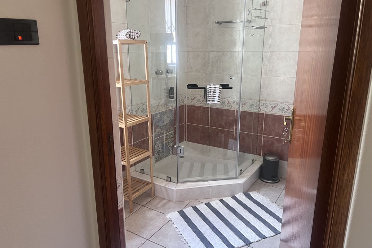 A functional bathroom featuring a corner glass shower enclosure with decorative tiled walls and neutral floor tiles.