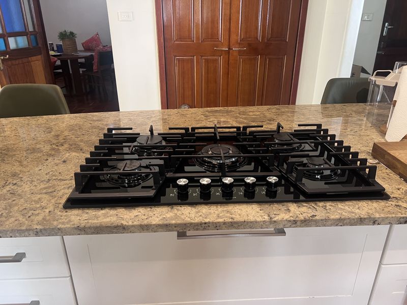 A modern kitchen island featuring a black five-burner gas cooktop set into a granite countertop with white cabinetry below.