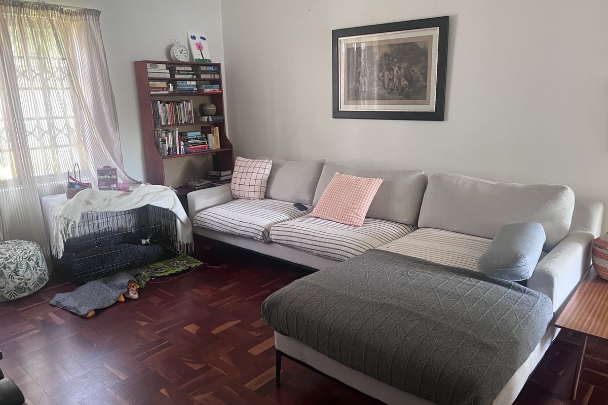 A comfortable living room featuring classic parquet flooring and a large window with security gate, providing a warm and inviting atmosphere.