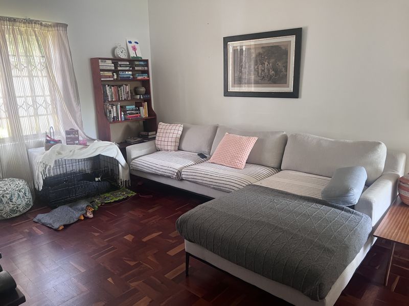A comfortable living room featuring classic parquet flooring and a large window with security gate, providing a warm and inviting atmosphere.
