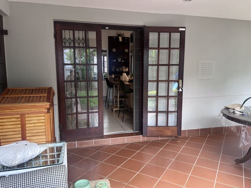 Covered patio area featuring terracotta floor tiles and wooden french doors providing access to the interior living space.