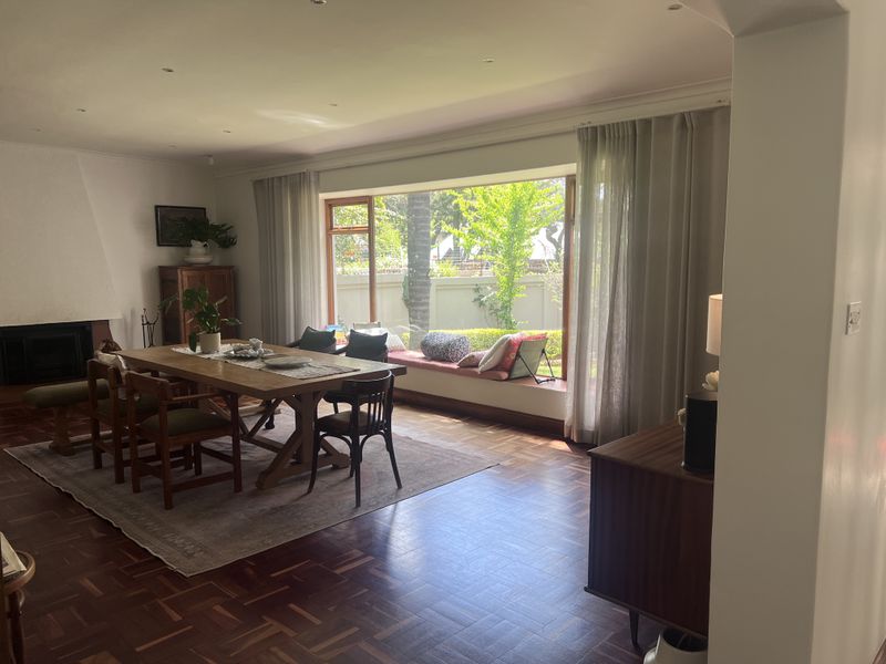Spacious dining room featuring rich parquet flooring, a built-in fireplace, and a large picture window with integrated bench seating overlooking the garden.