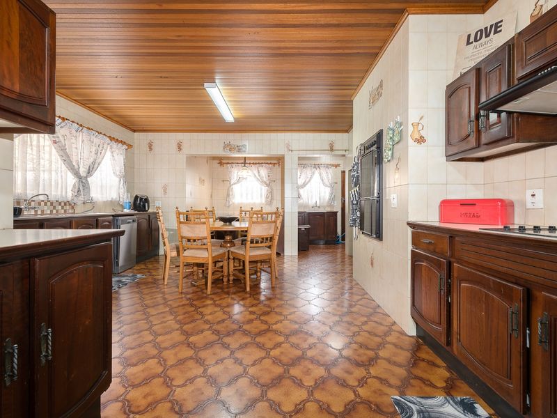 Spacious open-plan kitchen and dining area featuring traditional wooden cabinetry, tiled flooring, and a wooden ceiling, offering a functional layout with potential for modernization.