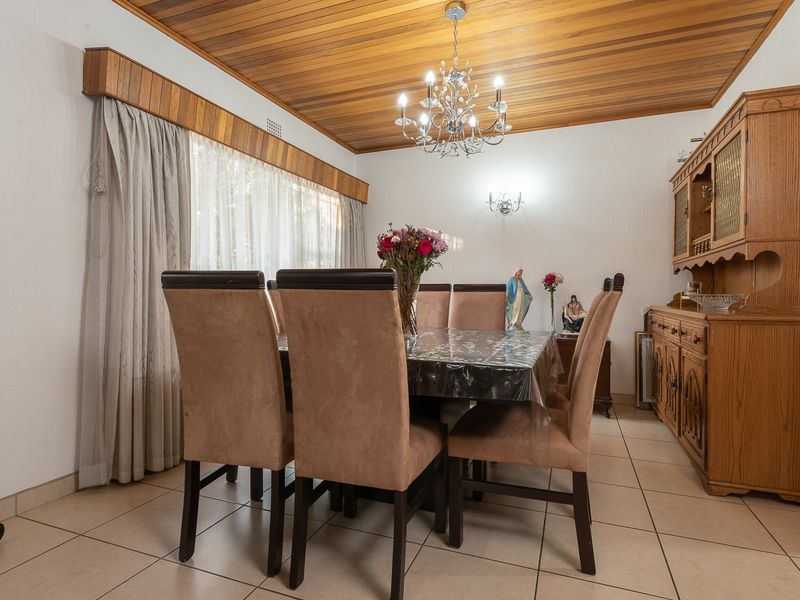A dining room featuring a warm timber tongue and groove ceiling, neutral ceramic floor tiles, and a classic chandelier.