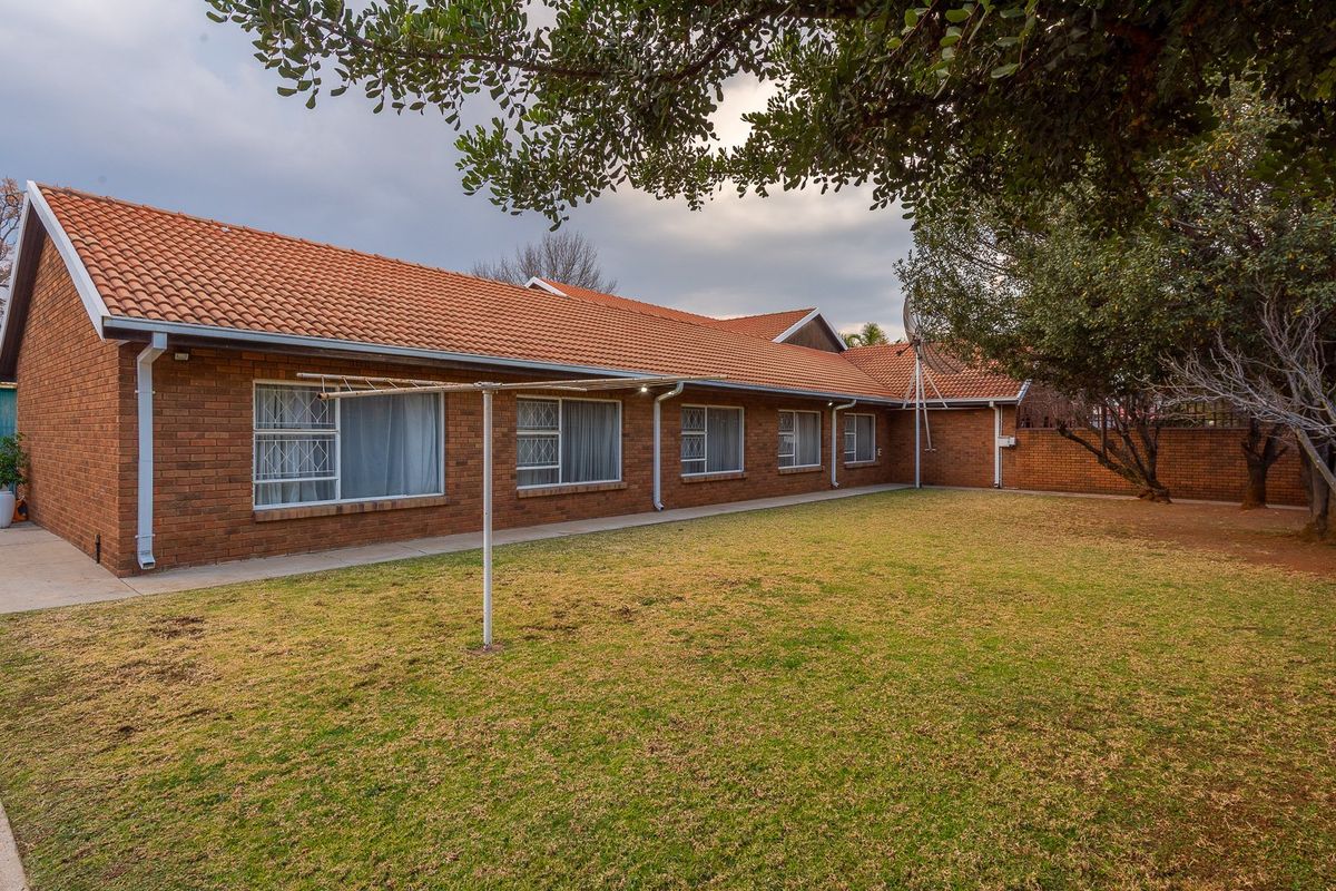 Rear view of a facebrick house featuring a terracotta tiled roof, security-barred windows, and a spacious lawn area with a concrete pathway.