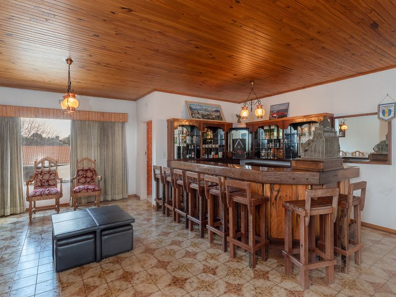 A dedicated bar area featuring a built-in wooden counter, timber-clad ceiling, and tiled flooring, offering a classic entertainment space.
